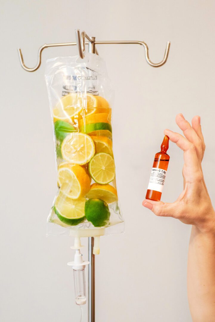 Hand holding vial next to citrus IV bag